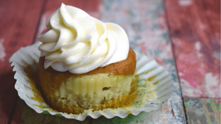 A close up of a single pumpkin cheesecake cupcake with the cupcake liner pulled down to reveal the cheesecake. 
