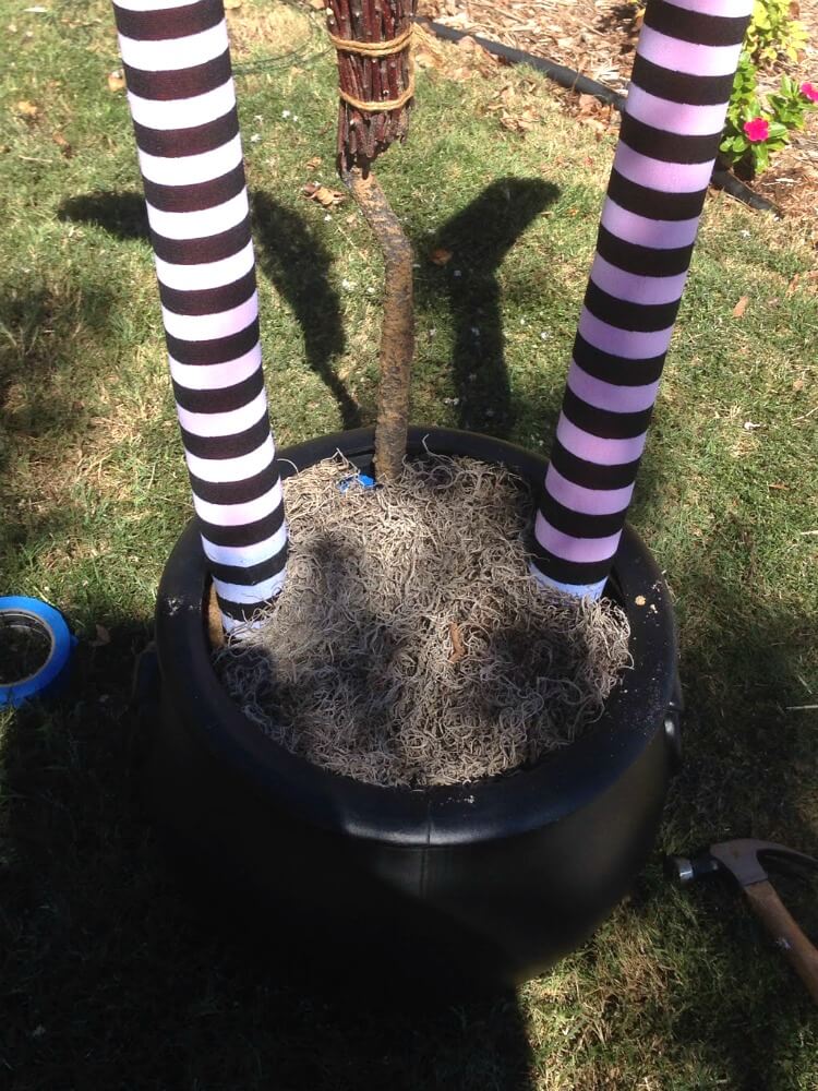 Add an upside down witch broom in the cauldron and tape it against one side of the cauldron. Then cover the top of the cauldron in spanish moss.