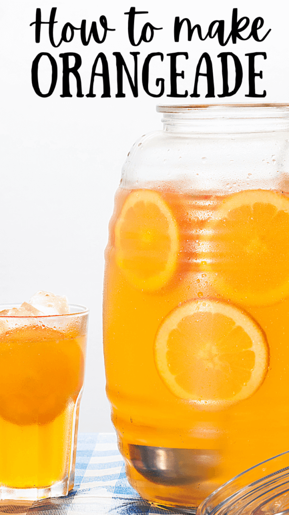 Title image with a close up of a pitcher of orangeade with orange slices floating inside with a glass nearby on a blue checked table. 