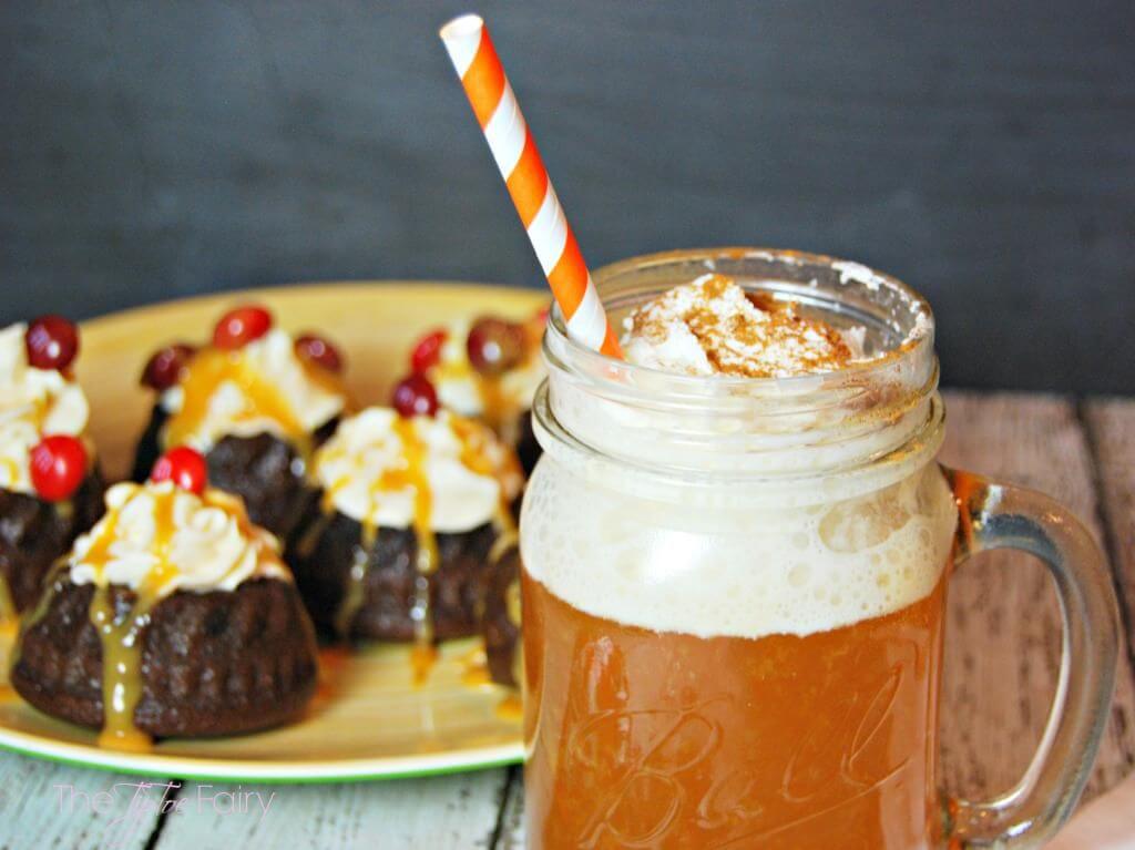 A mason jar of mulled apple cider in front of chocolate caramel mini cakes. 