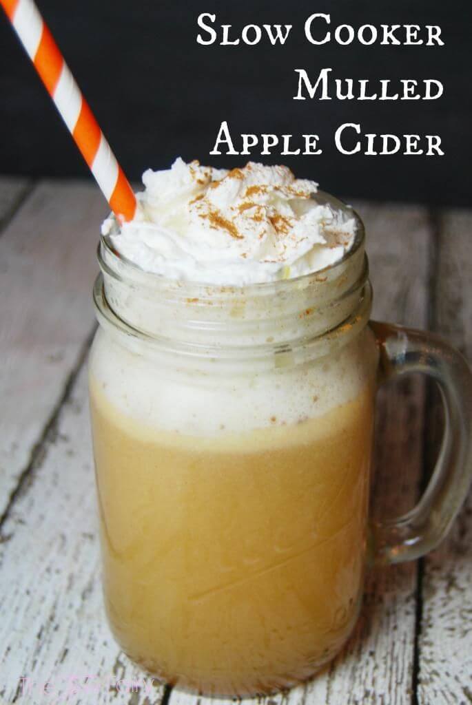 A mason jar mug full of mulled apple cider topped with whipped cream, cinnamon, and a straw. 
