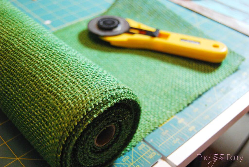 A roll of green burlap ribbon on the cutting mat with a rotary cutter.