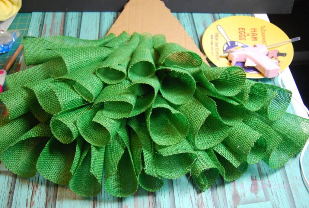 In process shot of the rolls of green burlap ribbon forming the christmas tree. 