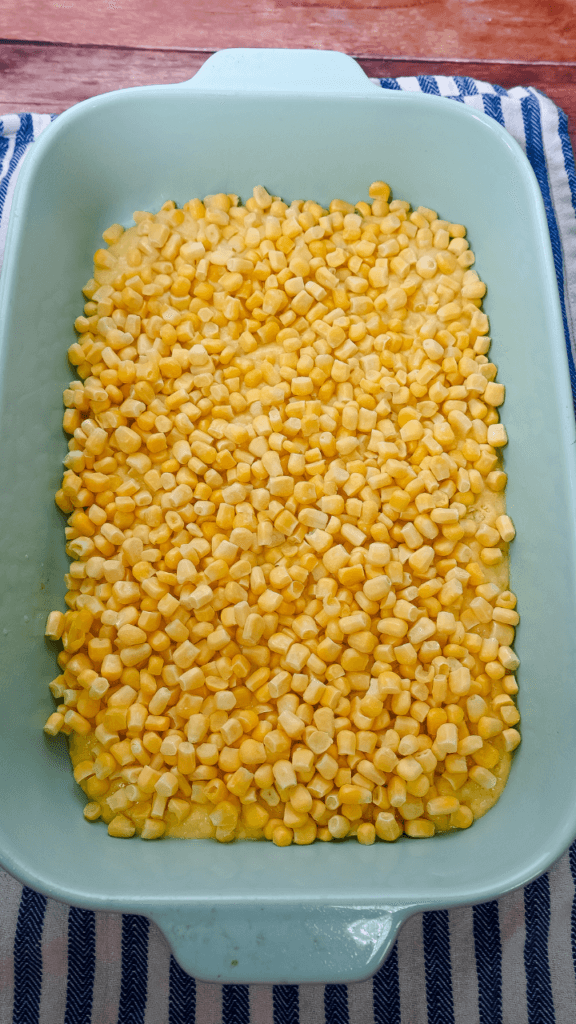 Second layer of Cowboy Brisket Casserole is frozen or canned corn on top of the cornbread layer before baking in a light blue casserole dish