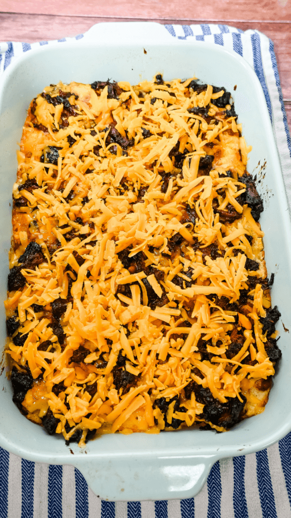 Fifth layer of Cowboy Brisket Casserole is shredded cheddar cheese in a light blue casserole dish