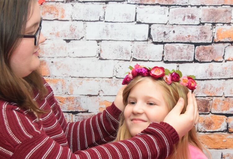 A big sister putting a candy flower crown onto her little sister's head.