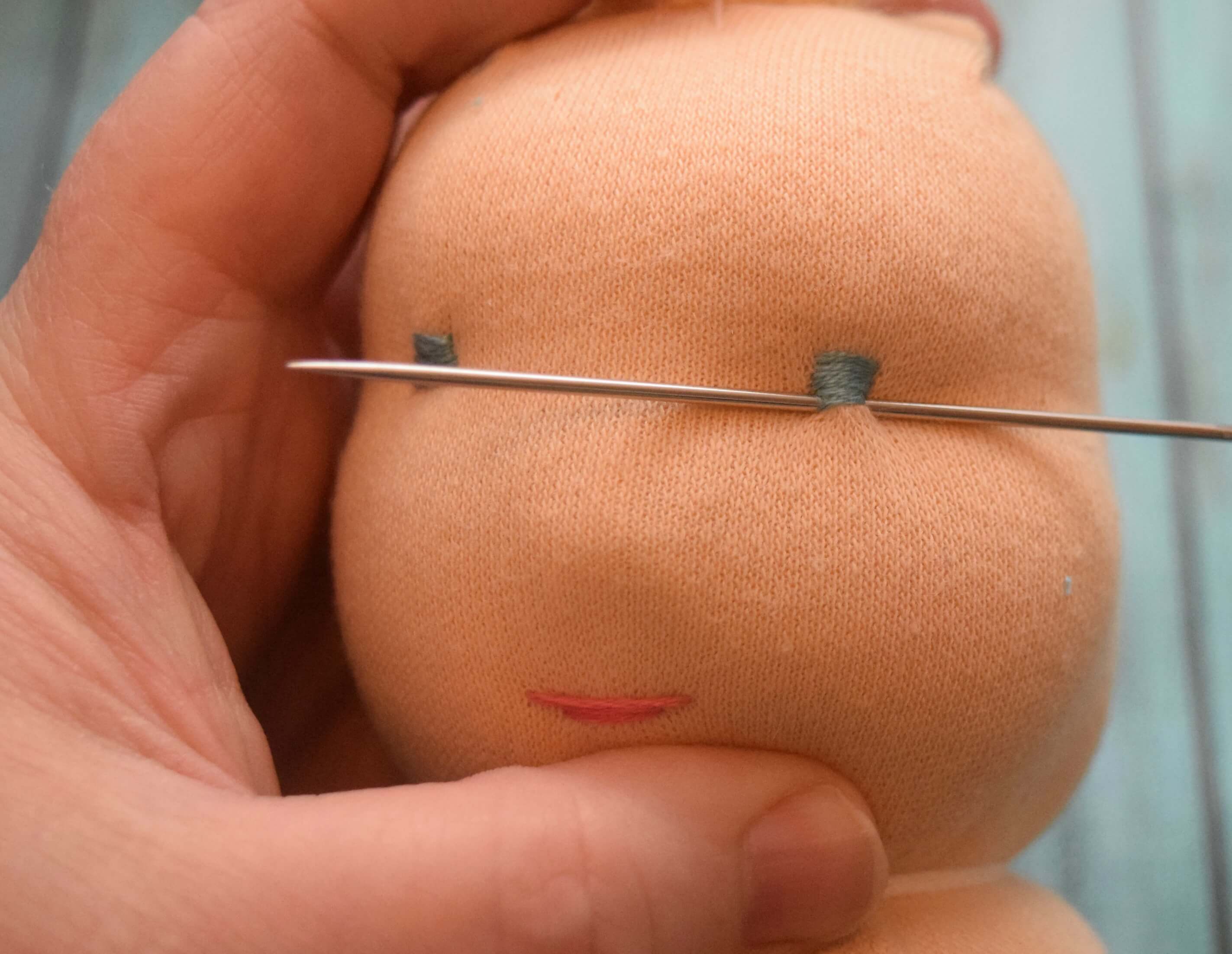 Using an embroidery needle to sew a satin stitch eye on the swaddle baby doll.