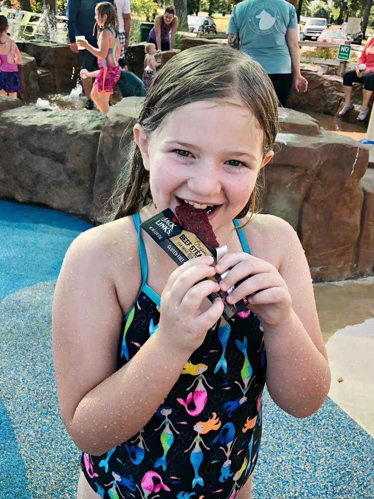 Tween eating a Jack Link's Bar at the splash pad. 