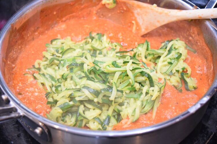 Tossing the zucchini noodles and shrimp into the creamy tomato sauce. 