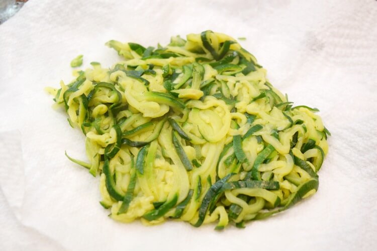 Removing the excess water from zucchini noodles with paper towels.