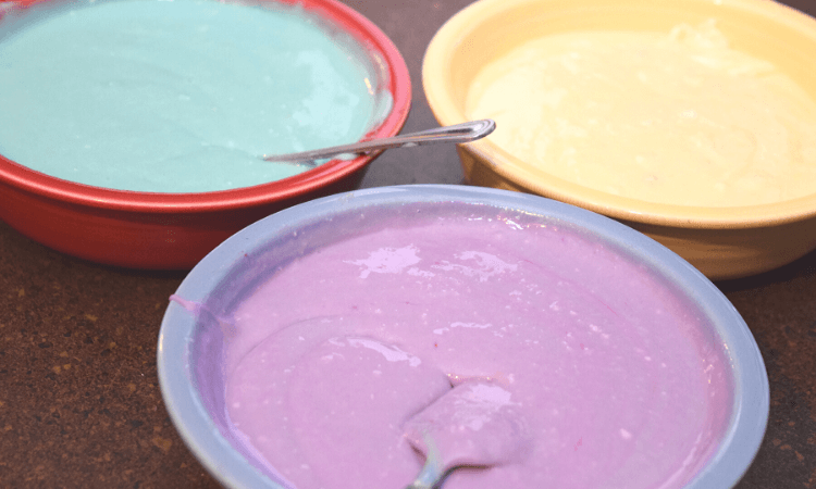 Three bowls of cheesecake batter in blue, fuchsia, and white.