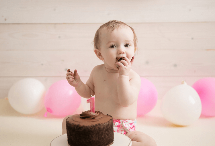 One year old baby girl eating a chocolate cake. Have a Smash Cake session with a themed-cake plate!