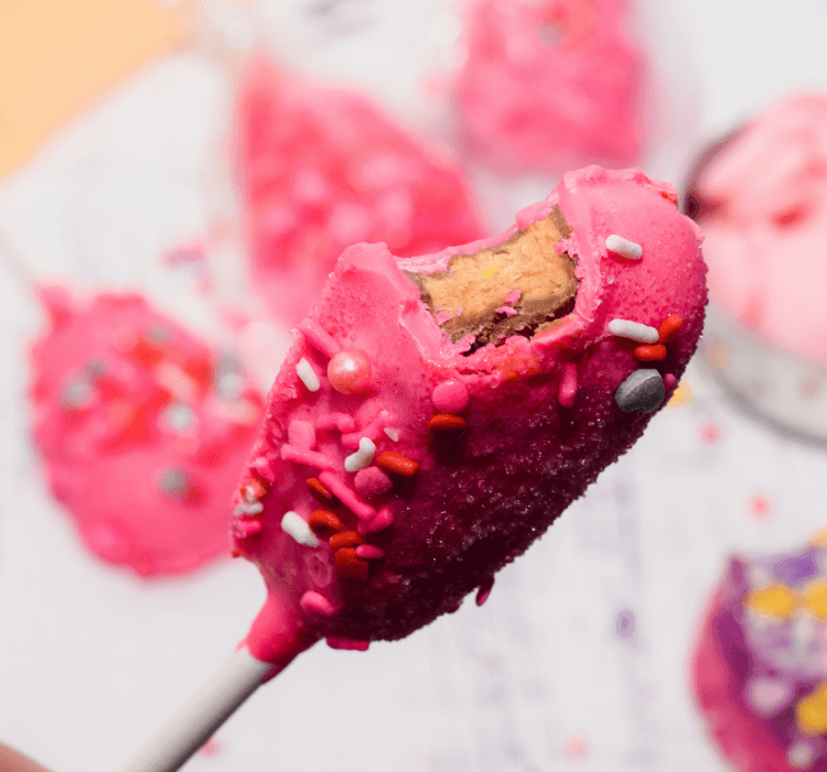 Heart shaped peanut butter cup dipped in pink candy melts and decorated with sprinkles with a bite taken out of it.