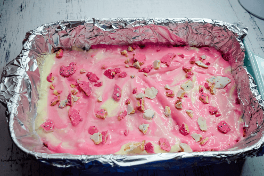 Bits of frosted animal cookies on top of the pink and white cheesecake batter. 