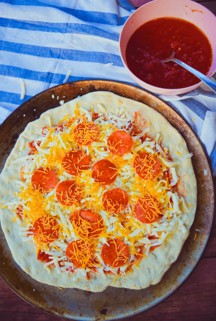 A finished pepperoni pizza before cooking with three cheeses and cheddar on top of the pepperonis. 