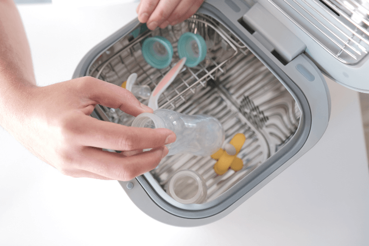 A top open view of the sanitizer with a woman's hand putting baby bottles into it.