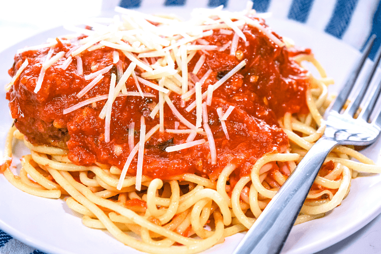 A white plate of spaghetti and meatballs covered in homemade sauce and fresh parmesan cheese.  