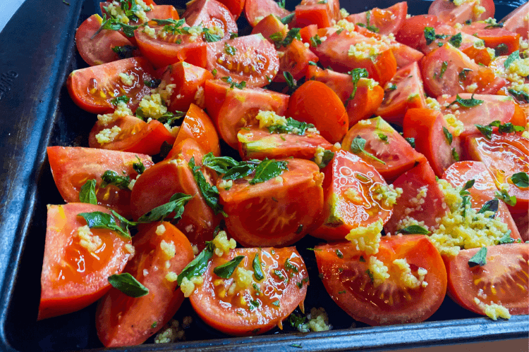 A baking sheet full of raw tomatoe quarters covered in herbs and minced garlic and olive oil. 