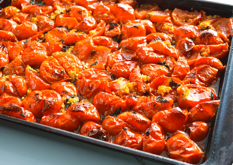 A pan of roasted tomatoes fresh out of the oven with little charred bits. 