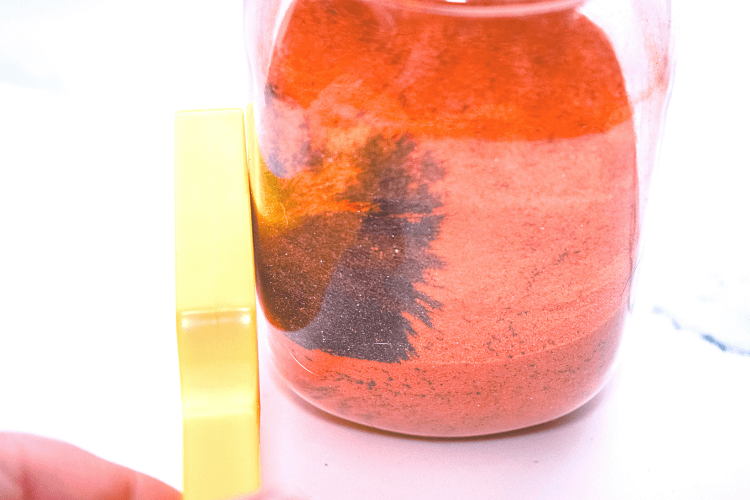 A yellow magnetic pulling the black iron filings out of orange colored sand through a plastic jar. 