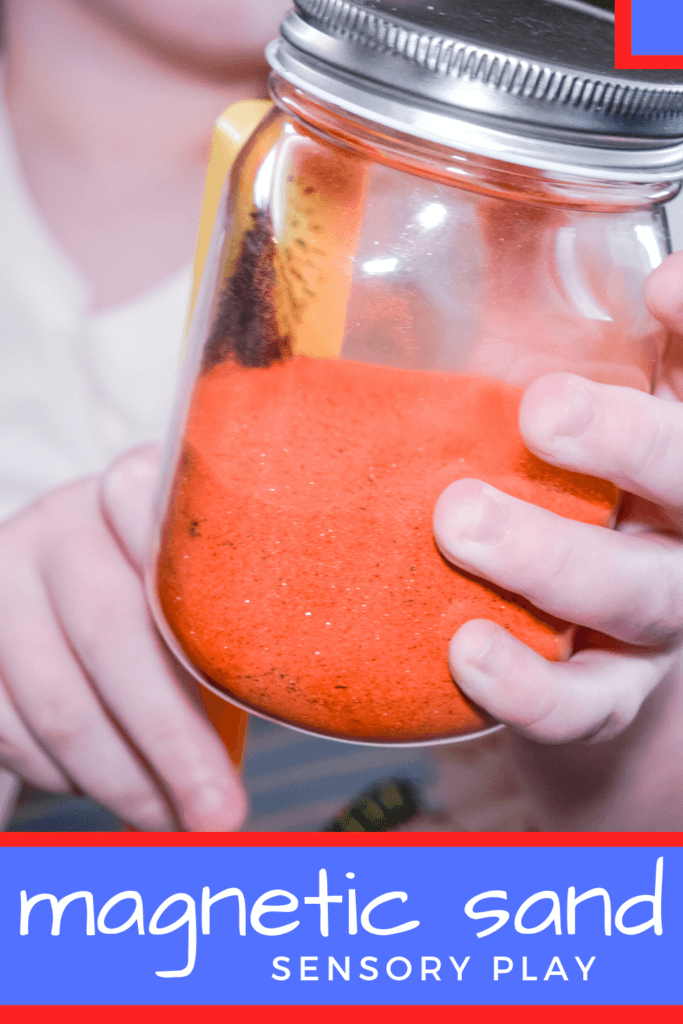 A child holding a magnetic wand and rubbing it on a plastic jar with orange sand to pull the iron filings out of the sand. 