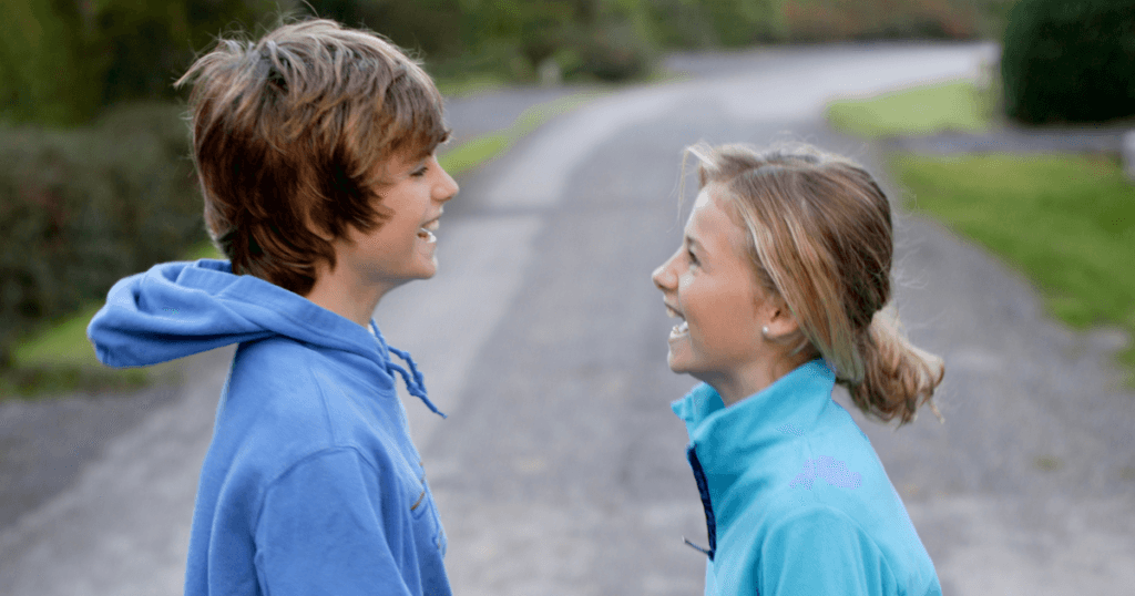 Tween boy and girl facing each other on a gravel road and laughing. 