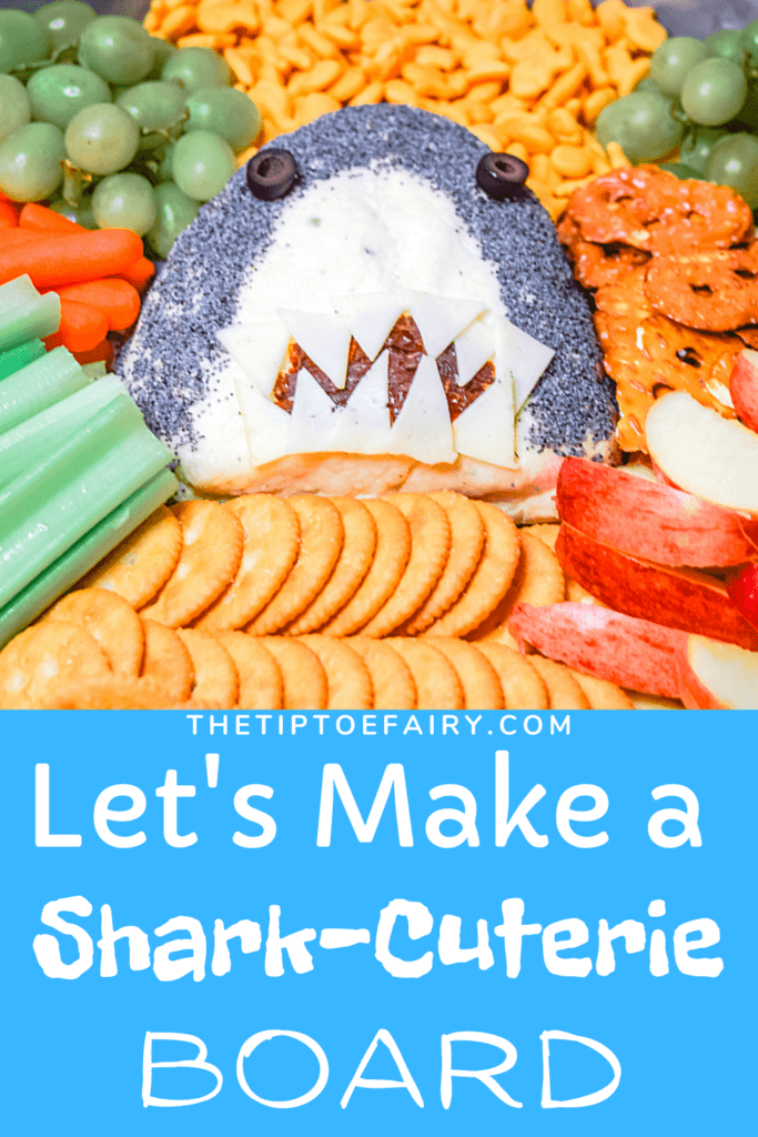 Close of a Shark Cheese Ball surrounded by crackers, veggies and fruit.