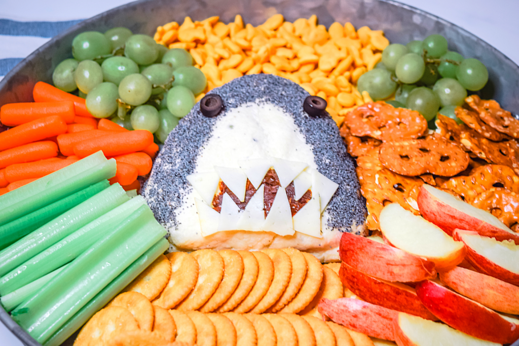 A Shark Cheese Ball surrounded by veggies, crackers, and fruit. 