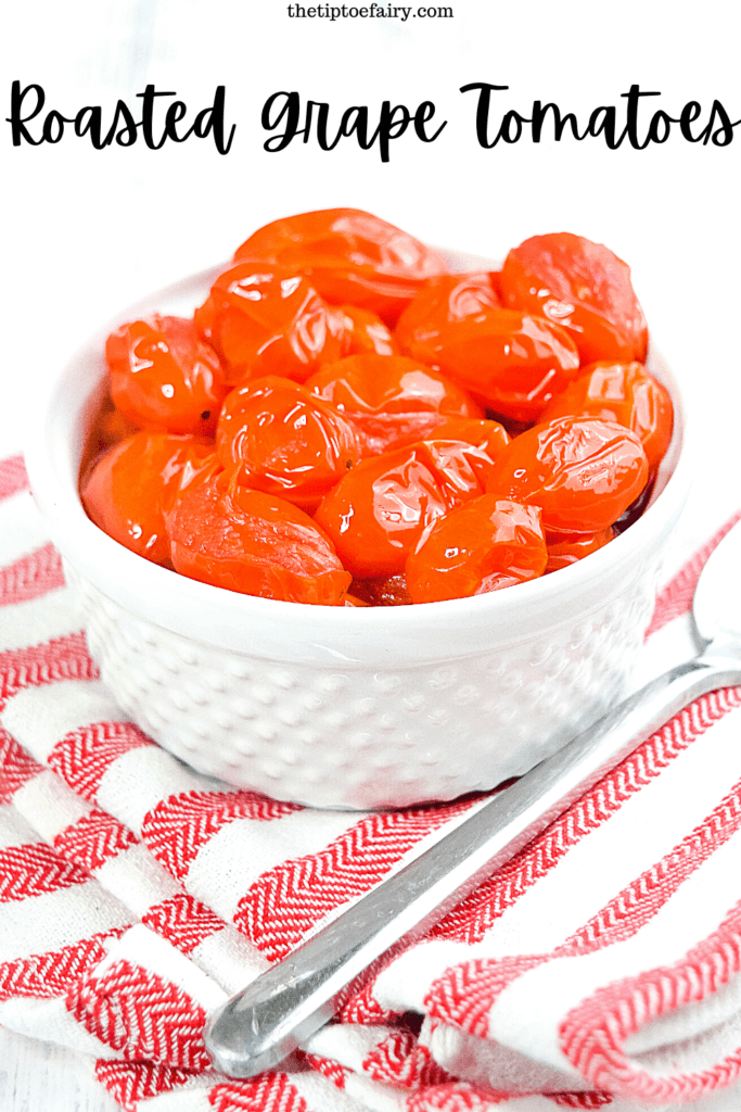 A white bowl filled with roasted grape tomatoes on top of a red and white striped kitchen towel. 