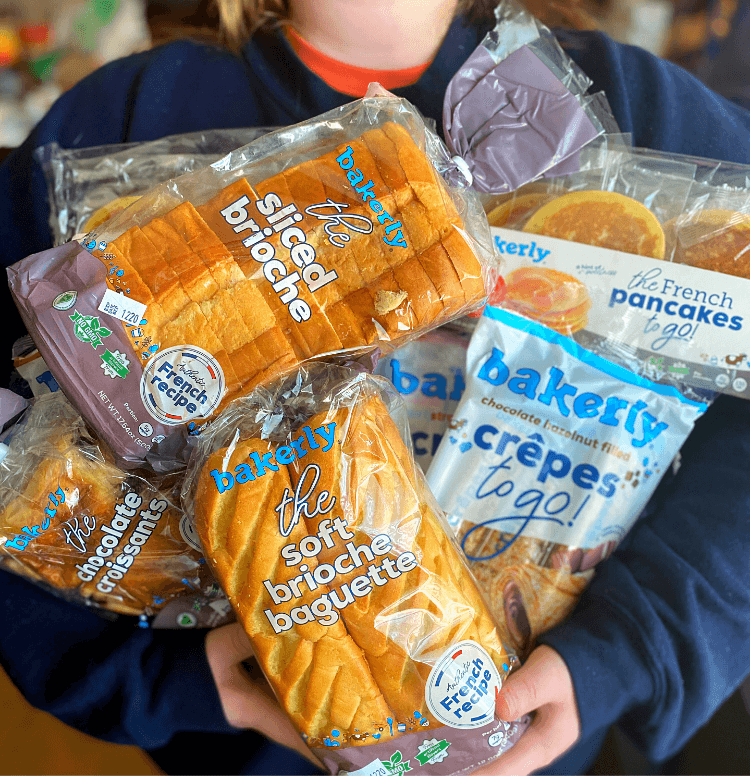 A young girl in a sweatshirt holding several bakerly bread products in her arms.