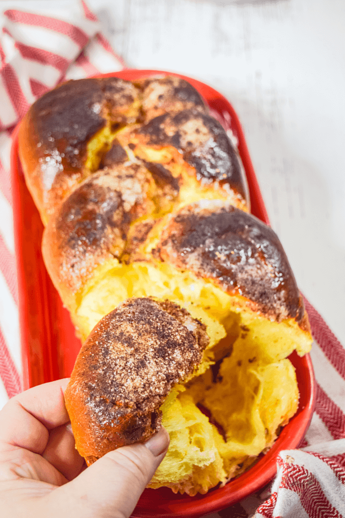 A hand pulling off a piece of the hand braided brioche bread made into cinnamon toast pull apart bread