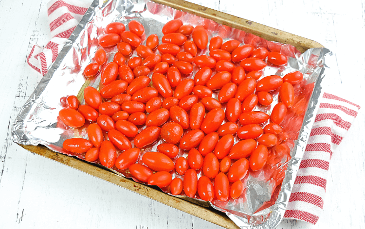 A cookie sheet covered in foil and topped with grape tomatoes drizzled in olive oil and salt. 