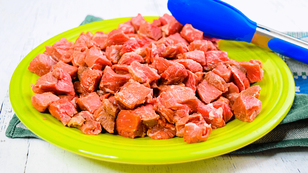 A green plate full of raw sirloin steak cut into cubes. 