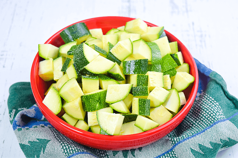 A red bowl full of cubed raw zucchini pieces. 