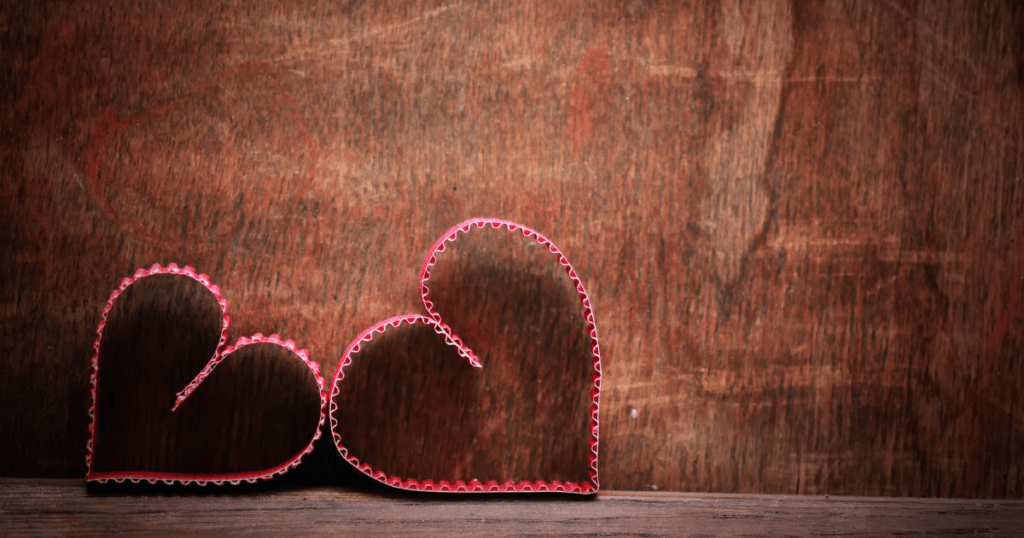 Pink corrugated cardboard hearts on a brown wood shelf. 