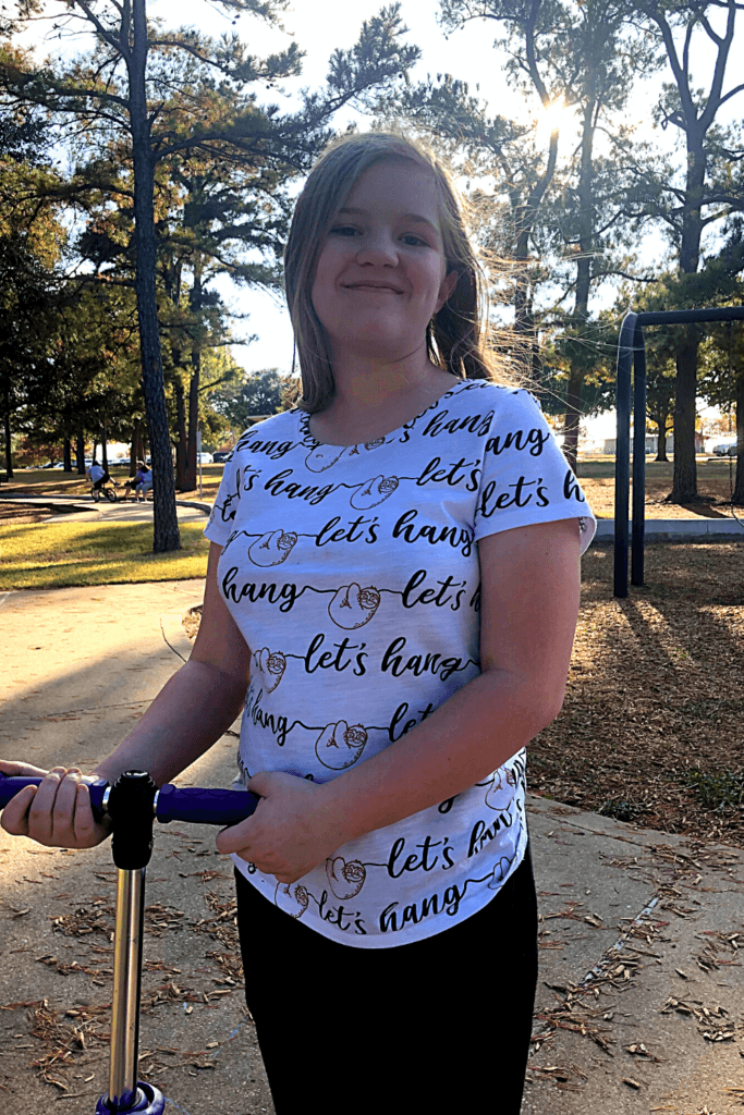 A preteen girl holding her scooter and smiling. 