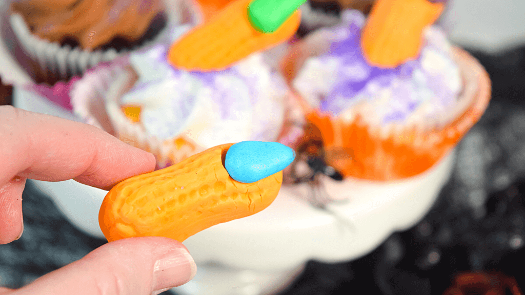 A hand holding a single witch finger candy with a blue fingernail