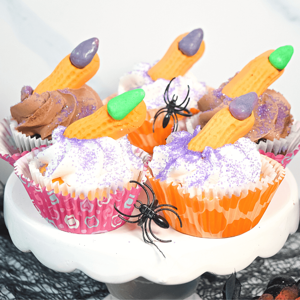 Close up image of five witch finger cupcakes with spider rings on a white pedestal