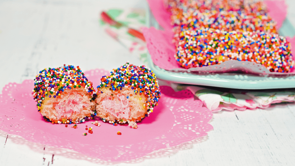 A fairy cake twinkie sliced open to reveal pink filling on a pink doily. 
