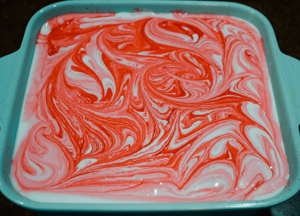 Swirls of red and white marshmallows left to firm up in a blue square casserole dish on a dark background