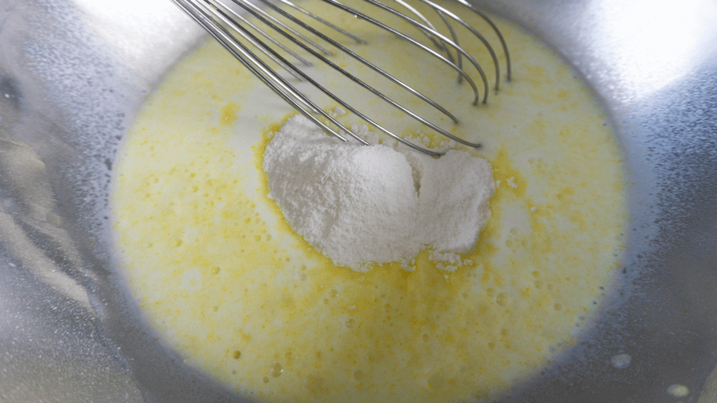A metal bowl and whisk with vanilla pudding mix and milk being whisked together. 