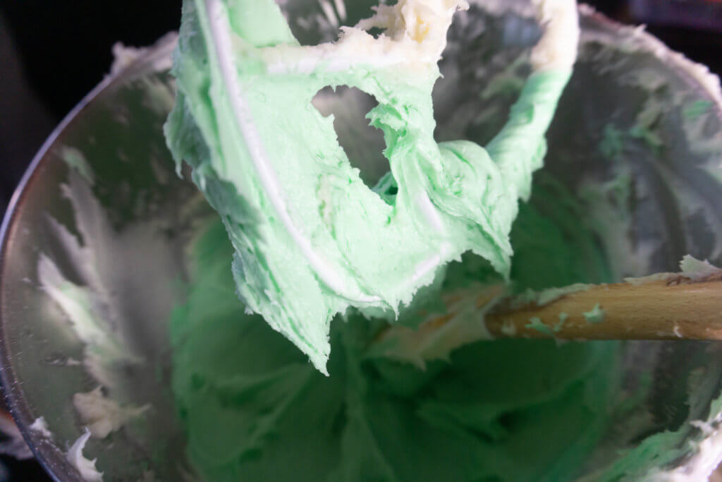 Close up of silver mixing bowl and paddle with green grinch sugar cookie dip. 