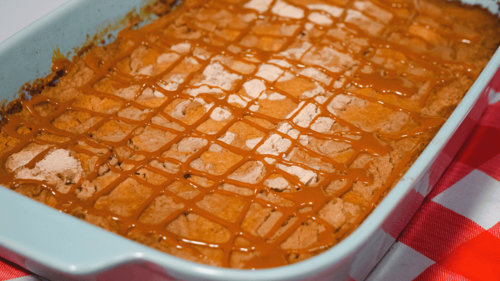 Dulce de lLeche Pumpkin Dump Cake in a light blue casserole dish drizzled with dulce de leche. 