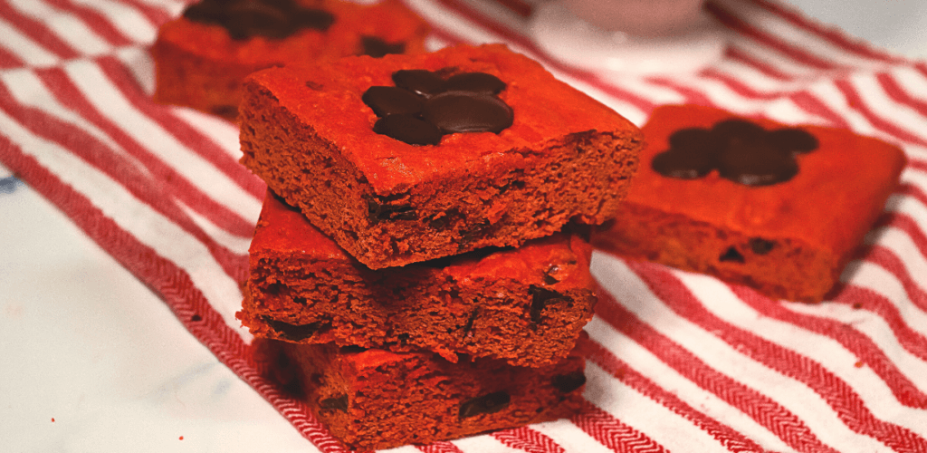 A red towel with a stack of 3 red velvet blondie bars with chocolate pawprints on top. 