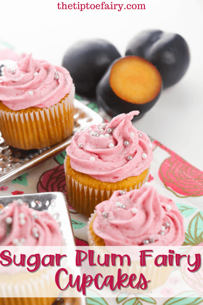 Title image for Sugar Plum Cupcakes with four cupcakes with pink frosting and silver sprinkles with 3 dark plums in the background, all on a rose tea towel. 