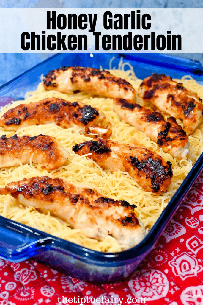 Blue casserole dish full of garlic butter angel hair pasta topped with honey garlic chicken tenderloins on a red placemat. 