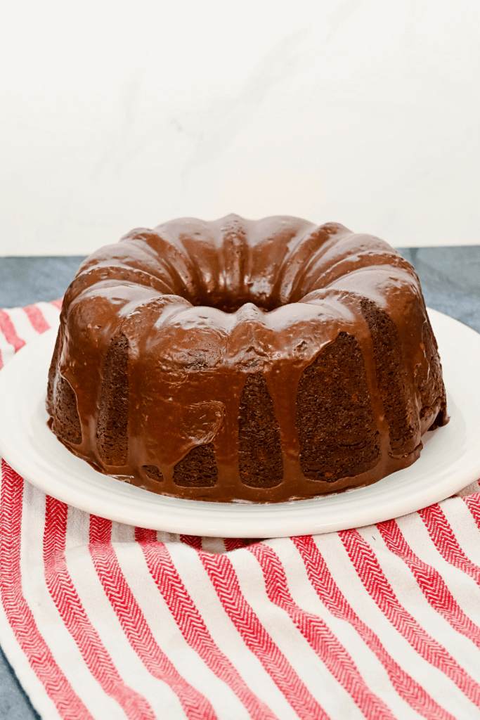 Hershey Bar Chocolate Cake on a white plate, drizzled in melted chocolate frosting, on a red striped towel. 