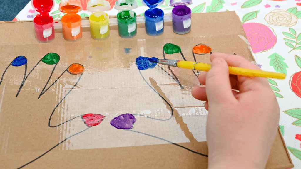 A child's hand painting fingernails on a piece of cardboard. 