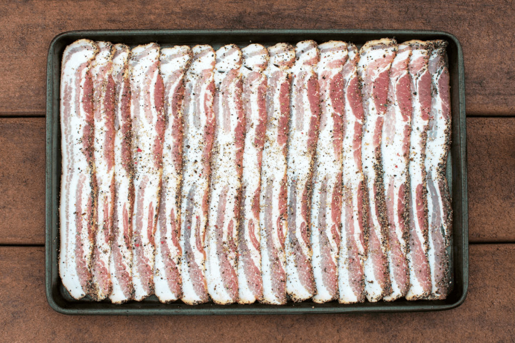 A sheet pan full of seasoning raw bacon before cooking in the oven.