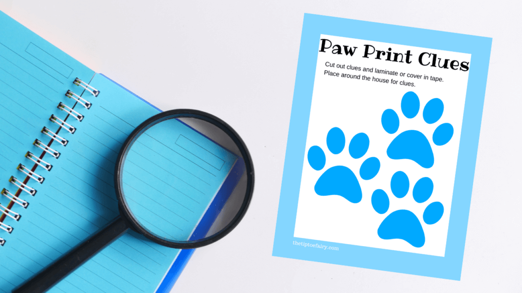 Blue notebook and black magnifying glass together on a white background with a mockup of the Paw Print Clues print out. 